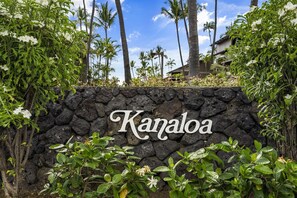 Surrounded by lush greenery and palm trees, Kanaloa features a stone wall with its name prominently displayed.