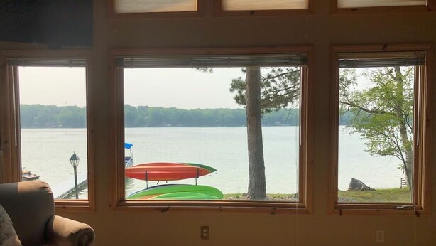 Une pièce dotée de grandes fenêtres donnant sur un lac, d’un fauteuil et d’une petite table.