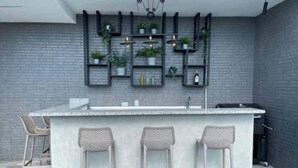 Una cocina moderna con barra, que presenta una pared de ladrillo gris, estantes colgantes con plantas y un lavamanos empotrado.