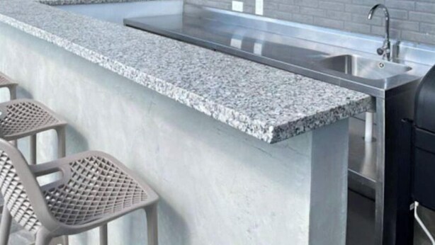 Una cocina moderna con encimera de granito, taburetes de bar, un lavamanos integrado y una estantería de pared con plantas en macetas.