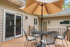 A patio with a table and chairs, a large umbrella, and a sliding glass door. - Dog-Friendly Three Little Birds Cottage on 3 Acres (Sturgeon Bay)