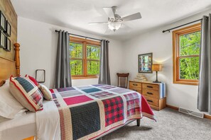 Un dormitorio con cama, cómoda, silla, ventilador de techo y ventanas amplias.