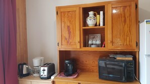 Eine kleine Küche mit Holzausstattung, einem Toaster, einer Kaffeemaschine, einer Mikrowelle und einem Kühlschrank.