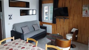 Ein gemütlicher Wohnbereich mit einer Couch, einem an der Wand befestigten Fernseher, einem Esstisch mit Stühlen und einem einzigartigen runden Tisch mit farbenfroher Tischplatte.