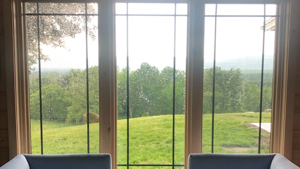 A room with two sofas facing a large window with a view of a green landscape. - Mid Century Modern Panoramic Mountain View House (New Paltz)