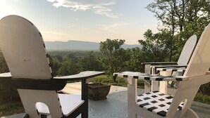 A seating area with two chairs and a table, overlooking a scenic landscape with trees and distant hills. - Mid Century Modern Panoramic Mountain View House (New Paltz)