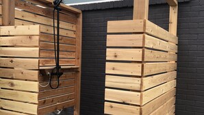 A wooden outdoor shower structure with a hose and showerhead, built into a house with a black brick exterior. - Mid Century Modern Panoramic Mountain View House (New Paltz)