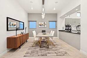 Un espace de salle à manger moderne avec une table centrale, des chaises blanches, une console en bois et des œuvres d’art abstraites accrochées aux murs.