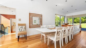 Un comedor moderno con una mesa y sillas blancas, piso de madera y un ventanal que ofrece vistas al exterior.