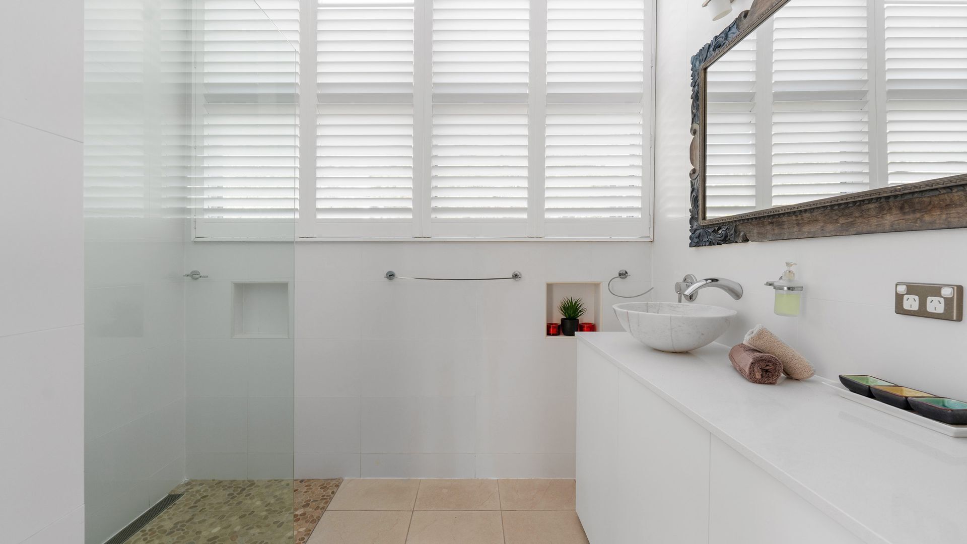 Un baño moderno con cabina de ducha de vidrio, un lavabo blanco con lavamanos de mármol y un espejo grande encima.