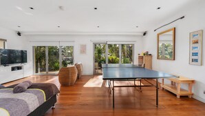 Amplia sala de estar con mesa de ping pong, televisión y un gran ventanal con vistas a un jardín.