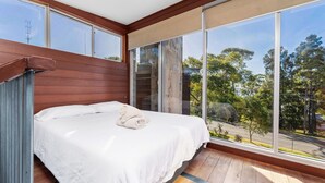Un dormitorio con un ventanal grande, cabecera de madera y una cama bien tendida con una toalla enrollada.
