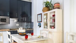 Eine moderne Küche mit dunklen Schränken, einem weißen Esstisch, Korbstühlen und einem Schrank mit Glastüren, der Küchenutensilien zeigt.
