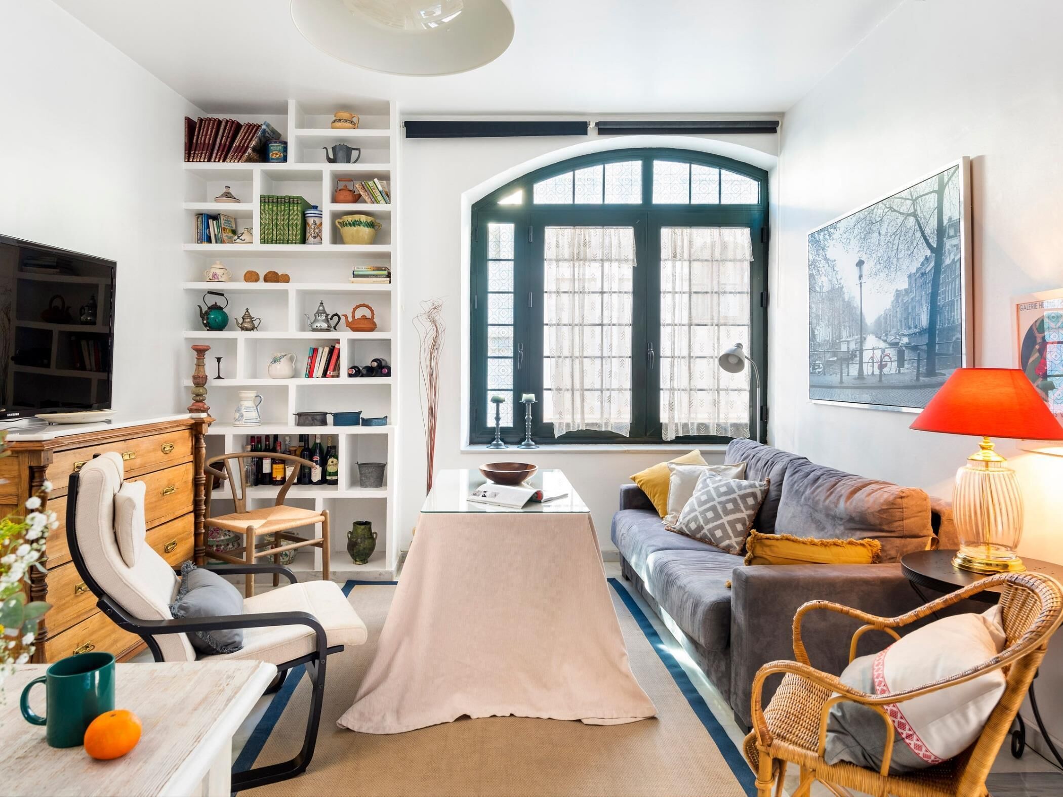 Ein Wohnzimmer mit Sofa, Couchtisch, Bücherregal, Fernseher und einem Fenster mit Vorhängen.