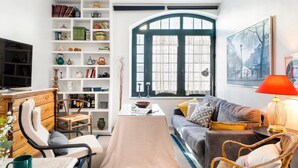 Ein Wohnzimmer mit Sofa, Couchtisch, Bücherregal, Fernseher und einem Fenster mit Vorhängen.