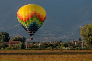 A hot air balloon with a rainbow pattern, flying over a rural landscape with houses and trees. - Casa Andreini, Capannori, Italy (Capannori)