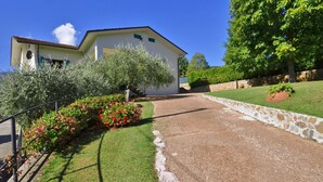 A house with a driveway leading to a white building, surrounded by greenery and a stone wall. - Casa Andreini, Capannori, Italy (Capannori)