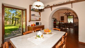 Un coin repas avec une table en marbre, des chaises, un panier de fruits et, au fond, une cuisine.