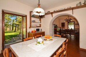 A dining area with a marble table, chairs, a fruit bowl, and a kitchen in the background.