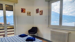 A bedroom with a bed, a chair, and a view of mountains through a large window. - Villa Canonica by Interhome (Varenna)