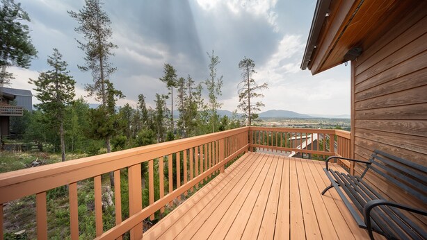 Une terrasse en bois avec un banc, entourée d’arbres et offrant une vue sur les montagnes lointaines.
