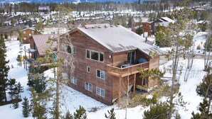 Une cabane en bois dotée d’un balcon, entourée d’arbres couverts de neige et avec des montagnes en arrière-plan.