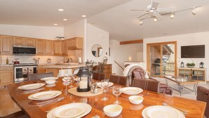 Une cuisine spacieuse avec des meubles en bois, une grande table à manger pouvant accueillir six personnes et un ventilateur de plafond moderne.