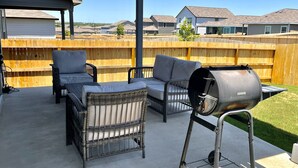 Un espace patio aménagé avec des meubles en osier, un barbecue et une clôture en bois.