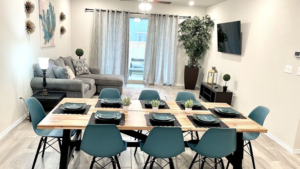 Un coin repas avec une table en bois dressée pour six personnes, entourée de chaises de couleur turquoise.