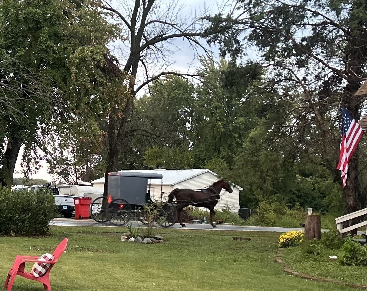 A horse-drawn carriage on a road with a house and trees in the background.