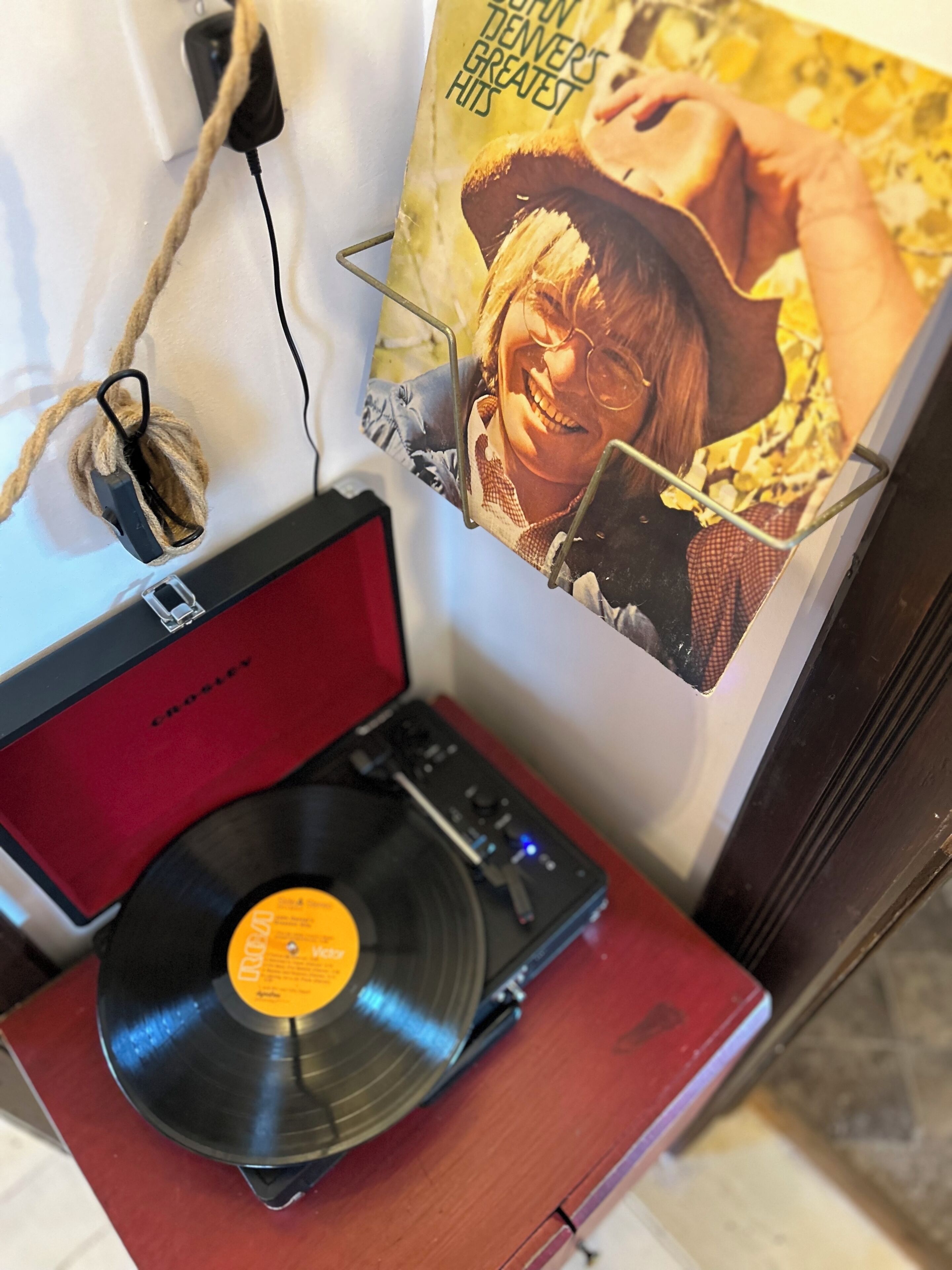 A turntable with a vinyl record, a power cord, and a poster on the wall.