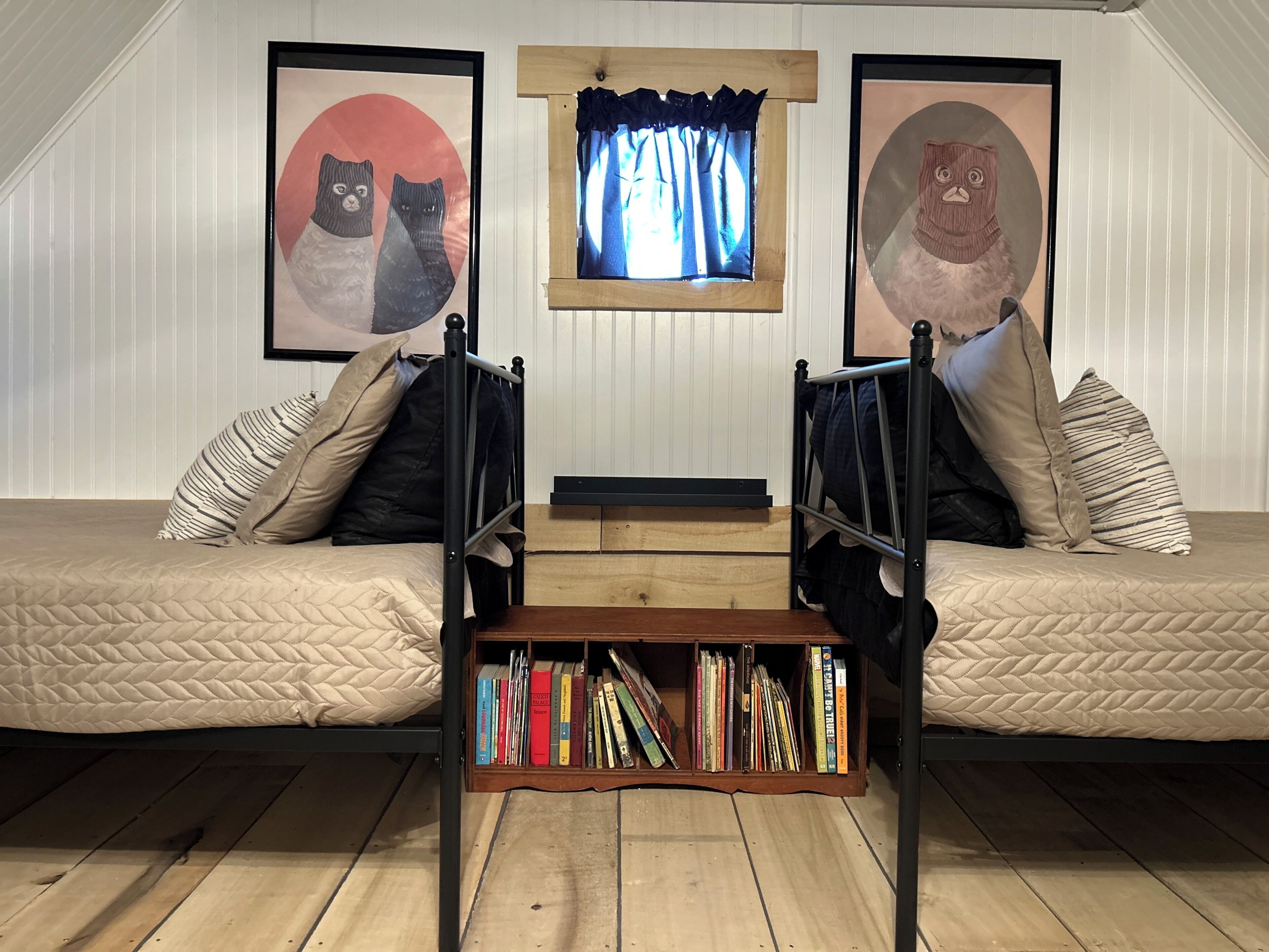 Une chambre à coucher aménagée dans un espace ouvert, avec deux lits superposés, une bibliothèque et deux portraits d’animaux encadrés.