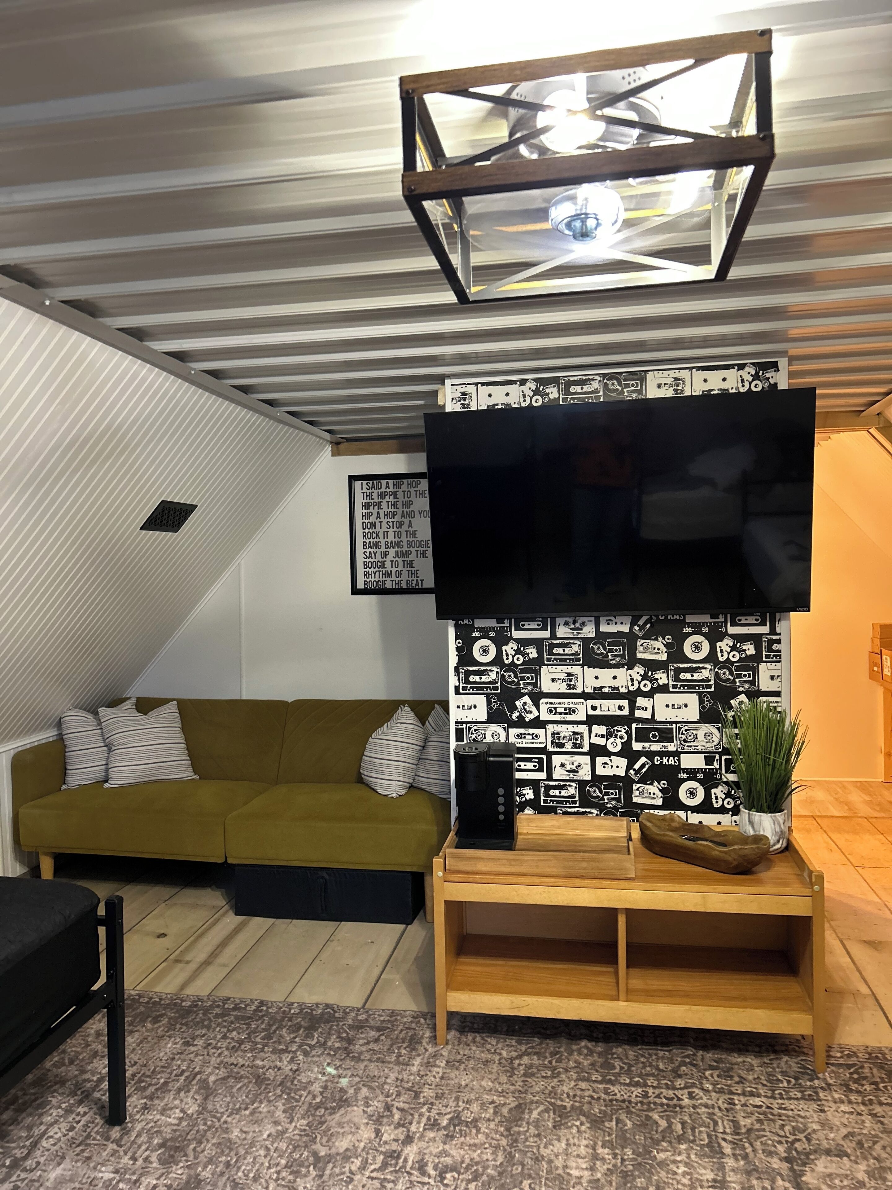 Una sala de estar moderna con un sofá verde, un mueble de televisión de madera y una pared decorada con cintas de cassette en blanco y negro.