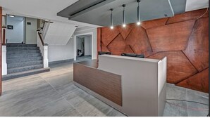 A reception area with a modern design, featuring a geometric wall pattern, a wooden reception desk, and a staircase with grey tiles. - Melour Resort (Tannersville)