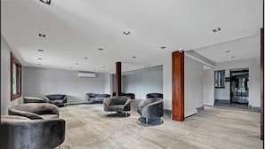 A spacious room with grey upholstered chairs, a wooden column, and a grey tiled floor. - Melour Resort (Tannersville)