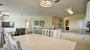 A spacious living room with a large white dining table, a ceiling fan, and a flat-screen TV mounted on the wall. - St Augustine Condo w/ Pool Access, Walk to Beach! (St. Augustine)