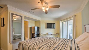 A bedroom with a bed, a ceiling fan, a TV, a refrigerator, and a bathroom visible through an open door. - Inviting St Augustine Studio - Walk to the Beach! (St. Augustine)