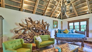Una stanza spaziosa con un soffitto in legno a vista, una grande scultura in legno appesa al muro, un letto con lenzuola blu e una poltrona verde.