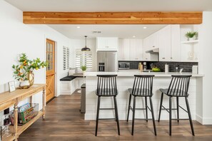 A modern kitchen with white cabinets, a stainless steel refrigerator, a black countertop, and three black bar stools. - Monterosa Green - BEST WALKABLE LOCATION in Charming Arcadia Lite w/ SPA! (Phoenix)