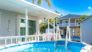 A pool area with a covered deck, a staircase leading to a second level, and a view of a neighboring building. - Anchor's Away: Discover Charm on the Canal, Swift Atlantic Access, Dockage & Above Ground Pool Await (Marathon)