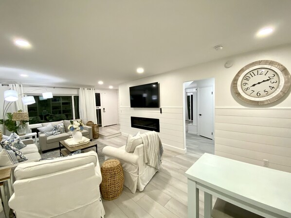 A modern living room with a flat-screen TV mounted on the wall, a large clock, and a sofa.
