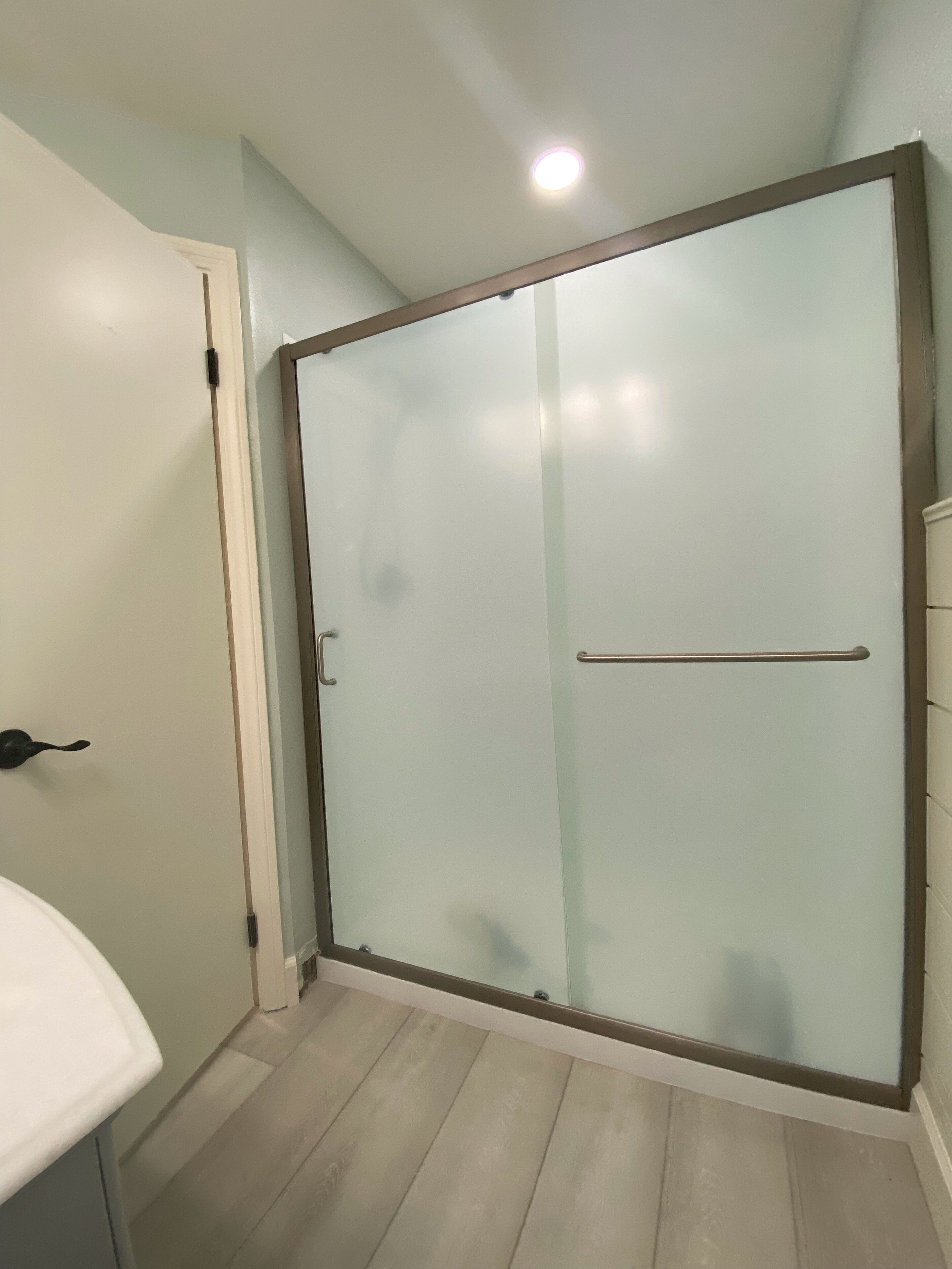 Ein Badezimmer mit Glastrennwand zur Dusche, einem weißen Waschbecken und hellem Holzboden.