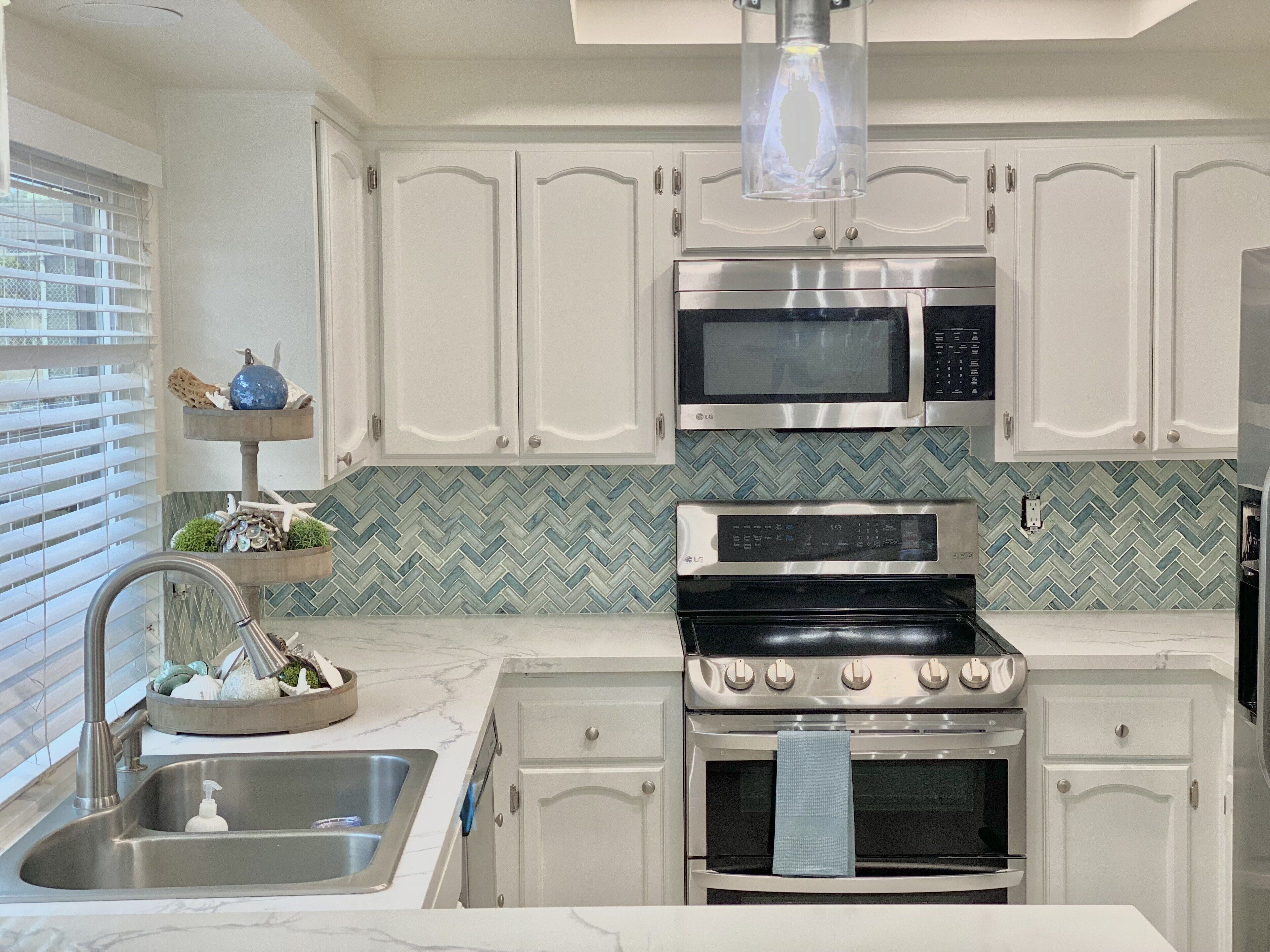 A modern kitchen with white cabinetry, a stainless steel stove, an LG microwave, and a herringbone-patterned backsplash.