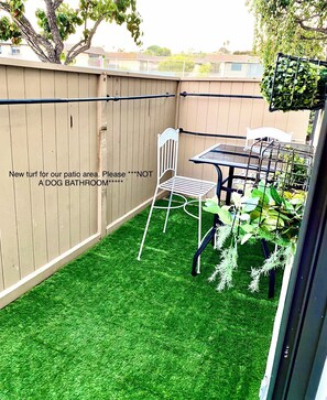 Un jardin avec une pelouse artificielle verte, une chaise en métal blanche, une table en métal et une autre chaise en métal blanche.