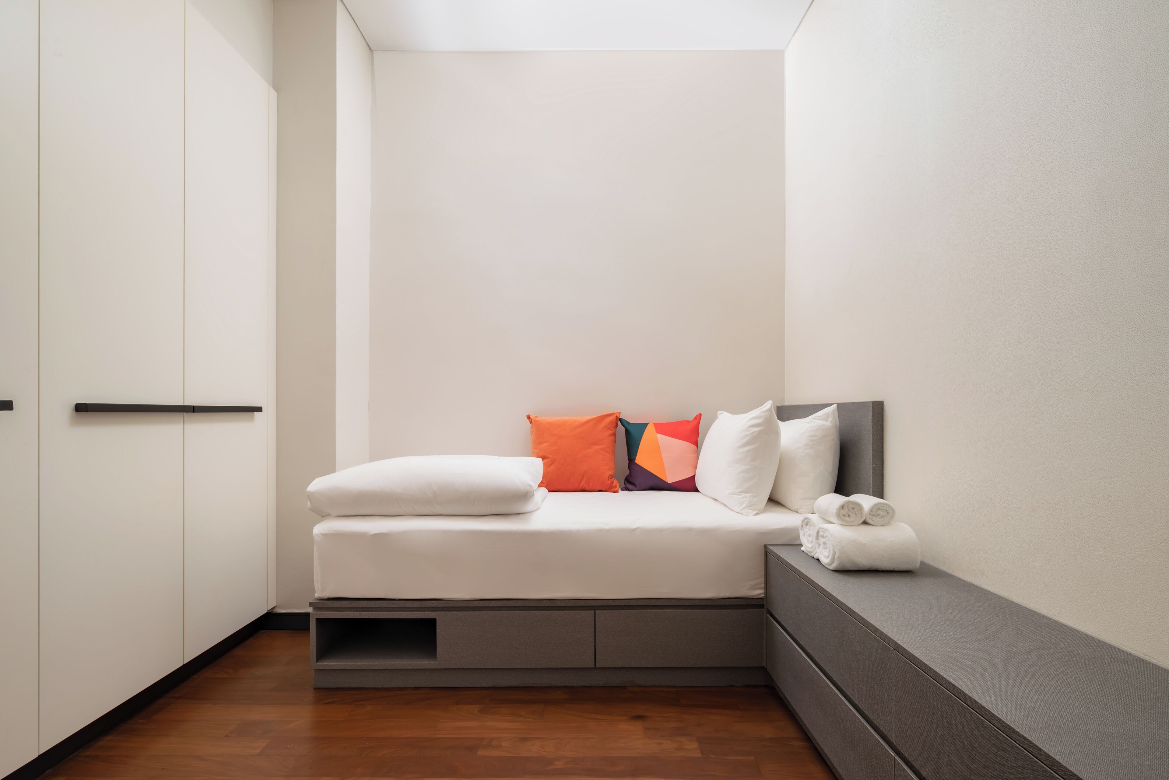 A small, modern bedroom with a bed, pillows, and a bench with towels.