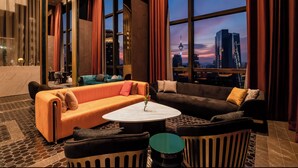 Un moderno hall de hotel con un amplio ventanal que ofrece vistas del horizonte de la ciudad, asientos cómodos y una mesa de centro de mármol.