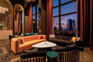 A modern hotel lobby with a large window offering a city skyline view, plush seating, and a marble coffee table.