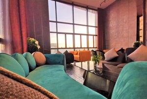 Een moderne woonkamer met smaragdgroene banken, een glazen salontafel en grote ramen met uitzicht op de stad.
