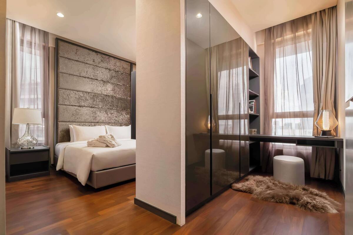 A modern bedroom with a large bed, a wooden headboard, a desk with a lamp, and a glass partition.