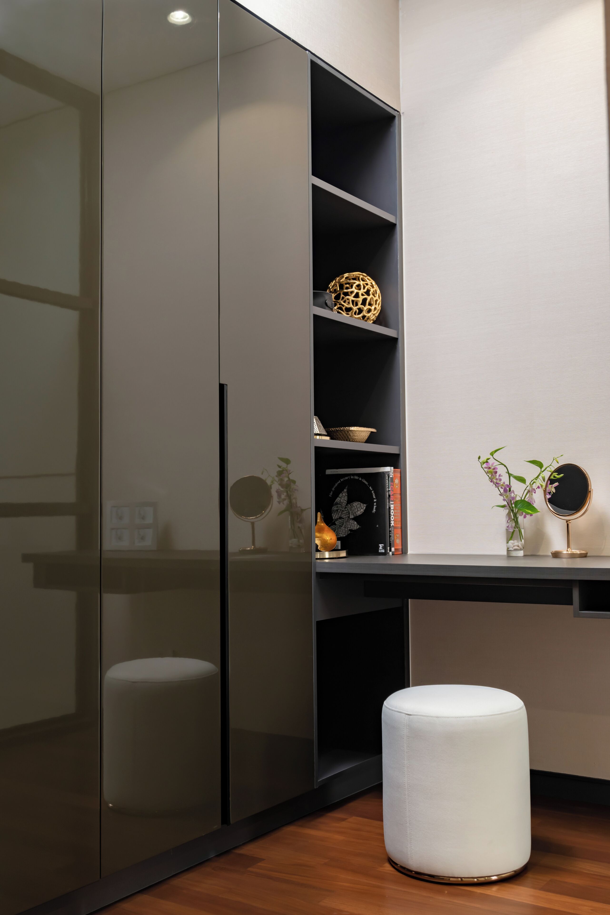 Una habitación moderna con un armario de puertas correderas, un otoman blanco, un pequeño estante con adornos y un espejo.